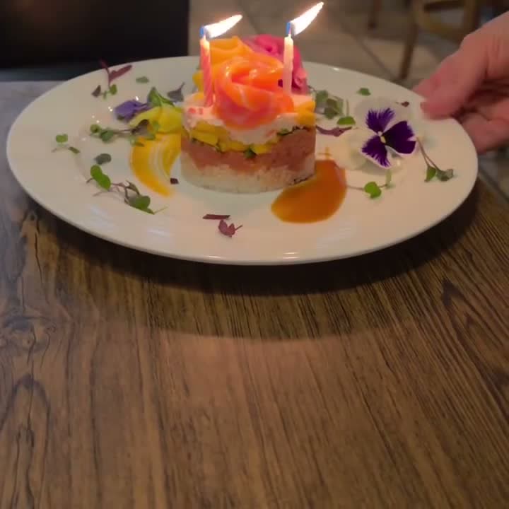 Starfish birthday sushi cake with salmon roses, two lit candles and flowers on the plate