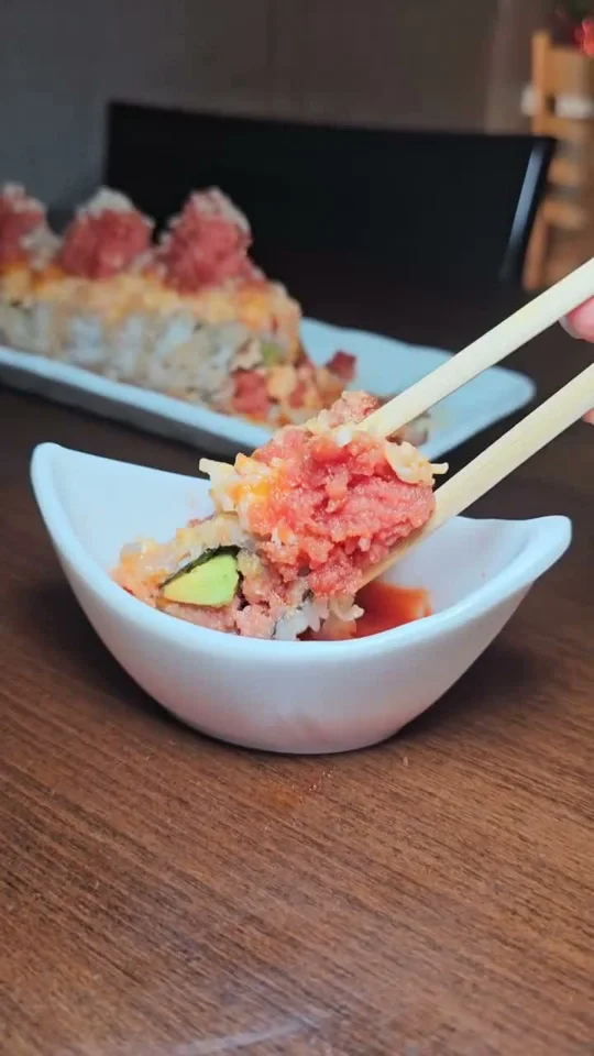 Chopsticks lifting a crunchy roll topped with spicy tuna